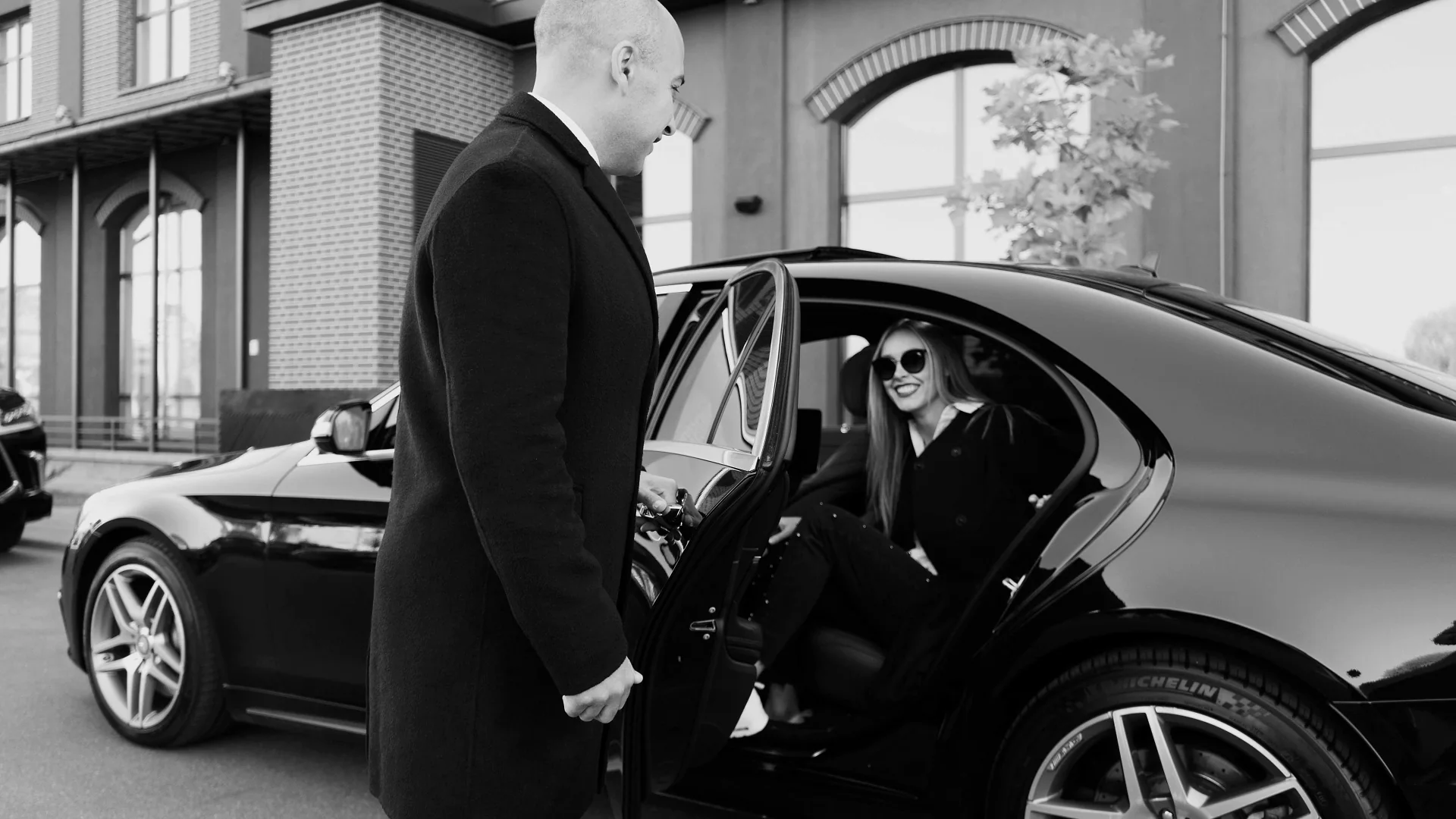 Professional chauffeur welcoming a passenger into a black luxury sedan