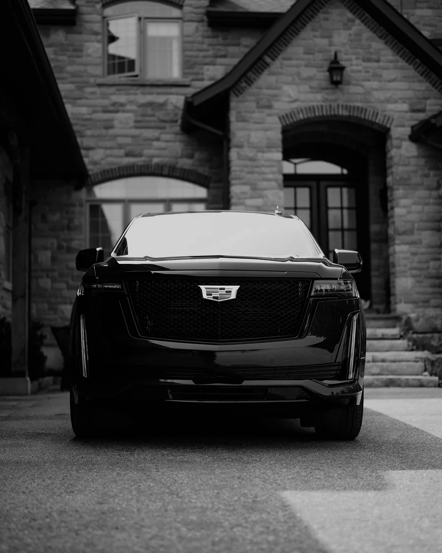 Professional chauffeur waiting beside a black 2026 Cadillac Escalade ESV